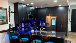 A modern kitchen with dark cabinetry, a central island with bar stools, and built-in appliances. - Las Palomas Phase 2 Coronado 1407 2 BR 2 BA (Puerto Peñasco)