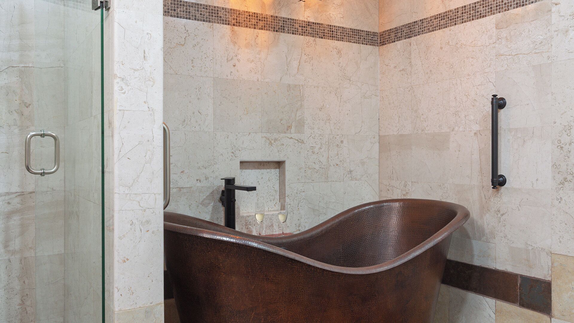 A bathroom with a freestanding bathtub, a glass shower enclosure, and a tiled wall with a decorative border.