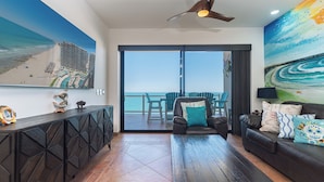 A living room with a view of the ocean, a ceiling fan, and a painting of a beach scene. - Las Palomas Phase 2 Coronado 1407 2 BR 2 BA (Puerto Peñasco)