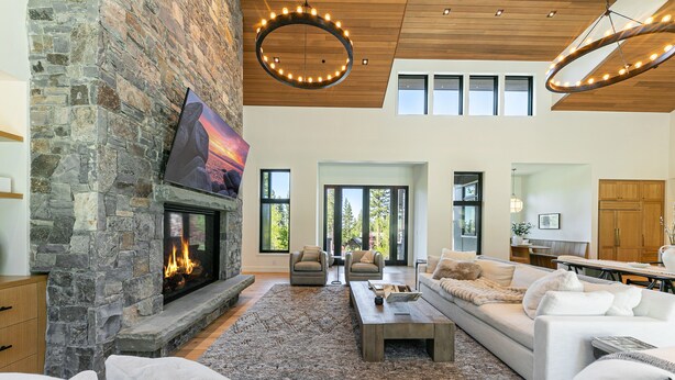 A spacious living room with a stone fireplace, modern furniture, and large windows.