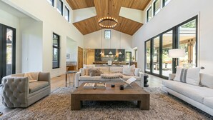 A spacious living room with a high ceiling, large windows, and a central coffee table.