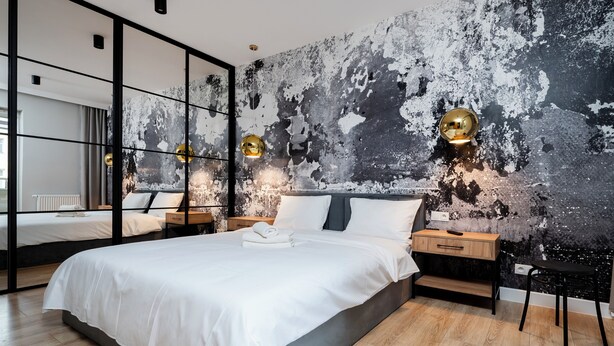 Een moderne slaapkamer met een groot bed, nachtkastjes en een unieke, verweerde wand.