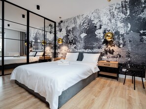 Une chambre moderne avec un grand lit, des tables de chevet et un mur au décor original, dont l’aspect vieilli est particulièrement réussi.