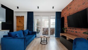 Een moderne woonkamer met een blauwe bank, een televisie bevestigd aan een bakstenen muur en een schuifdeur die leidt naar een buitenruimte.