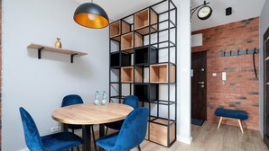 Een moderne eetruimte met een ronde houten tafel, blauwe fluweelstoelen, een zwarte metalen kast en een hangende pendantlamp.
