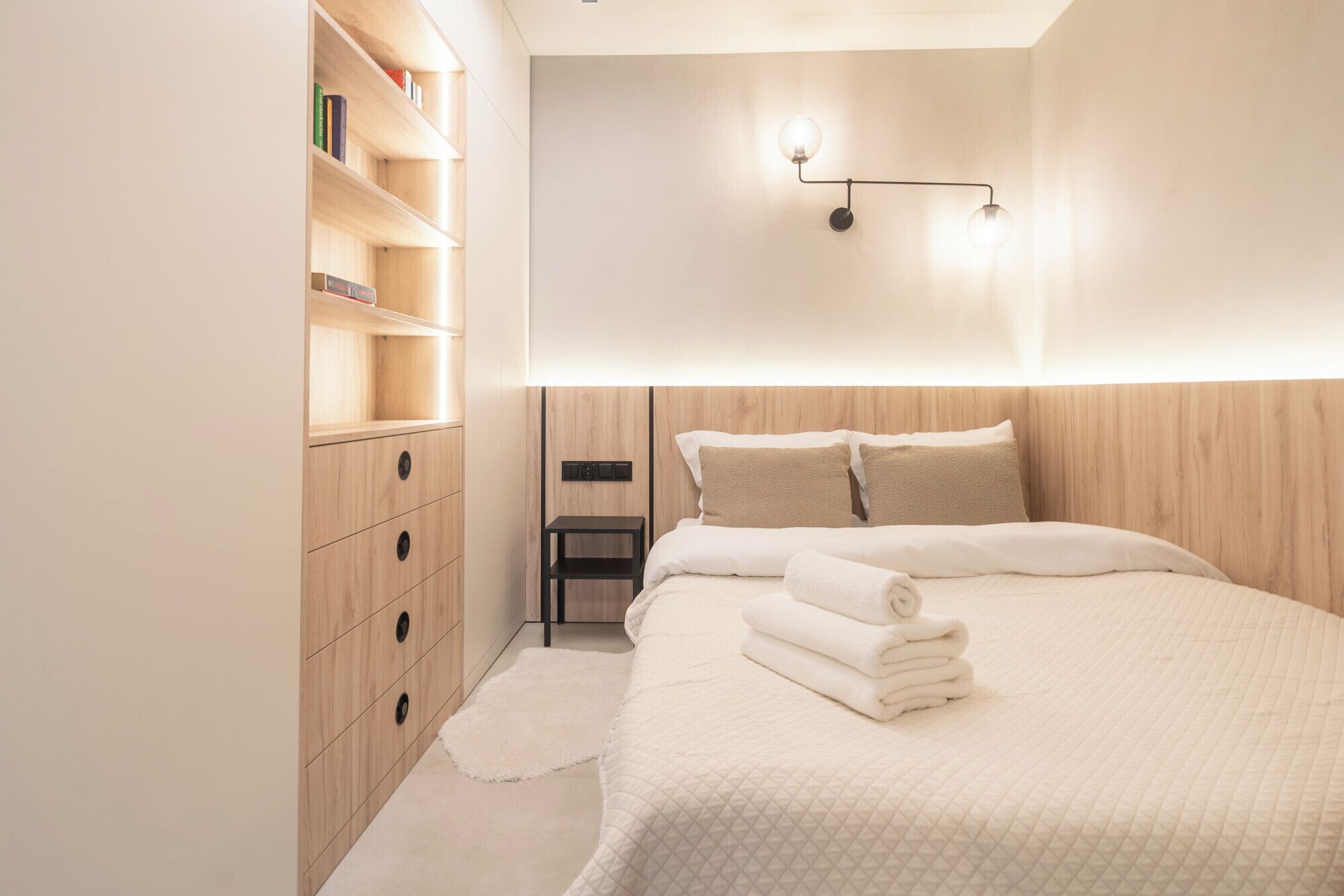 Quarto moderno com cabeceira de madeira, mesa de cabeceira e estante embutida.