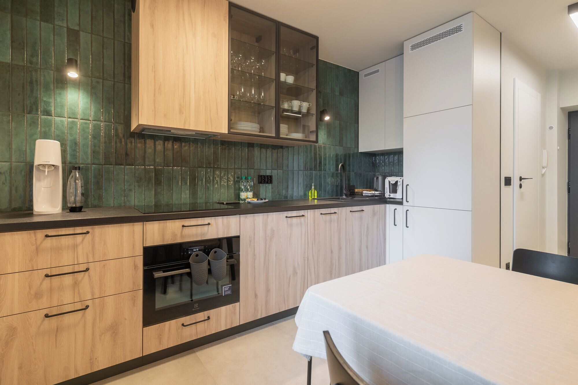 A modern kitchen with wooden cabinets, a built-in oven, and a dining area with a table.