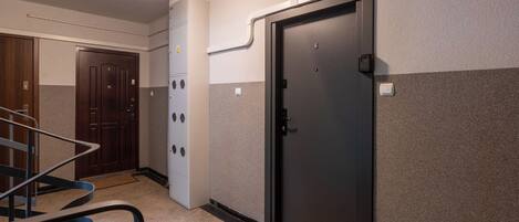 A hotel room with a dark door, a white wall with a textured pattern, a wooden door, and a metal staircase railing.