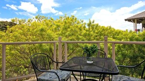 A balcony with a table and chairs, overlooking a lush green landscape and a clear blue sky.