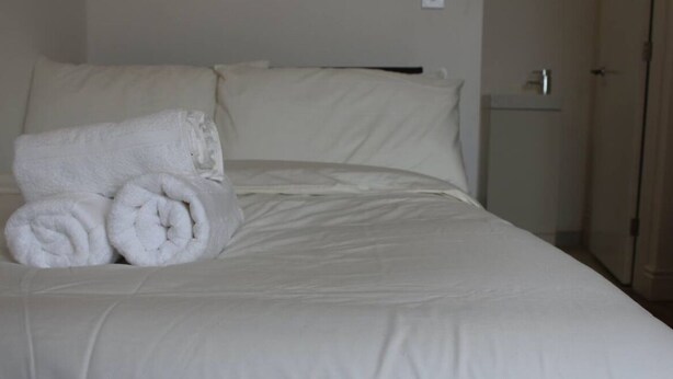 Een opgemaakt bed met witte lakens en opgerolde handdoeken aan de zijkant.