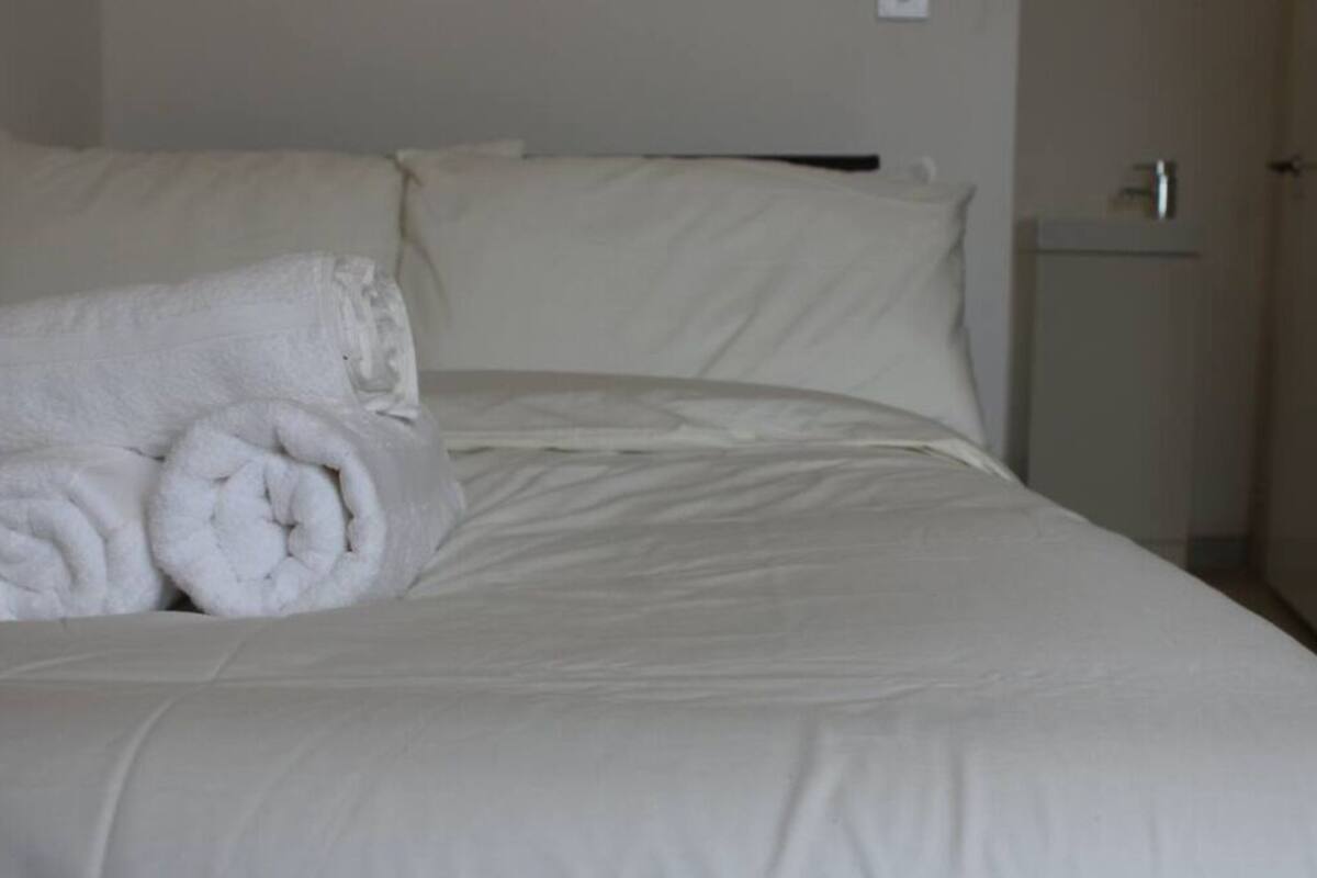 A neatly made bed with white linens and rolled towels on the side.
