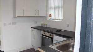 Een keuken met witte kastjes, een zwart aanrecht, een raam met zonwering en een roestvrijstalen spoelbak.