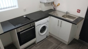 Een compacte keuken met een inbouwoven, een wasmachine, een spoelbak en een raam met zonwering.