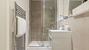 Un baño moderno con ducha de vidrio, lavamanos blanco y barra para toallas.
