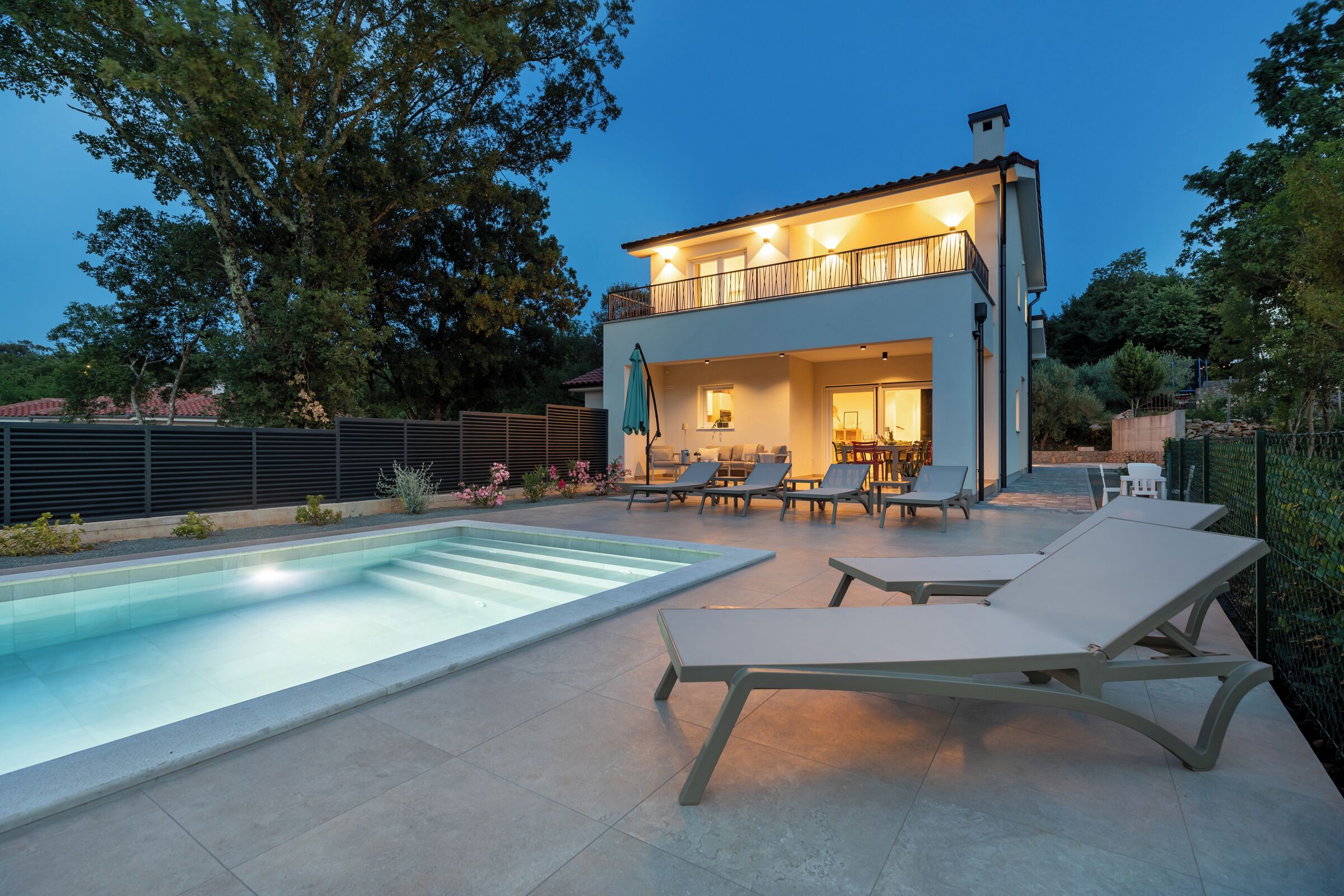 A modern two-story house with a swimming pool, outdoor seating, and a balcony.