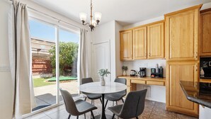 Une cuisine avec des meubles en bois, une table à manger avec des chaises et une porte-fenêtre coulissante donnant sur un patio.