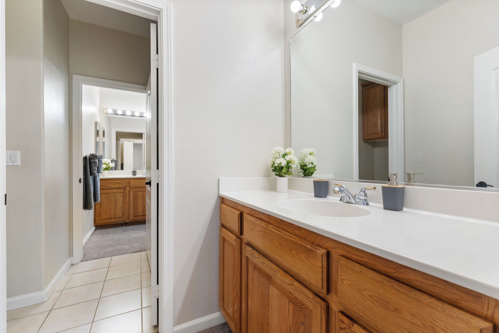 Un bagno moderno con un grande specchio, un mobile contenitore in legno e un lavandino bianco.