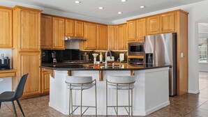 Une cuisine moderne avec des meubles en bois, des appareils en acier inoxydable, un îlot central doté de tabourets et un sol carrelé.