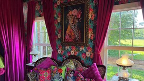 Quarto com cama, almofadas coloridas, um quadro e vista para o verde lá fora.