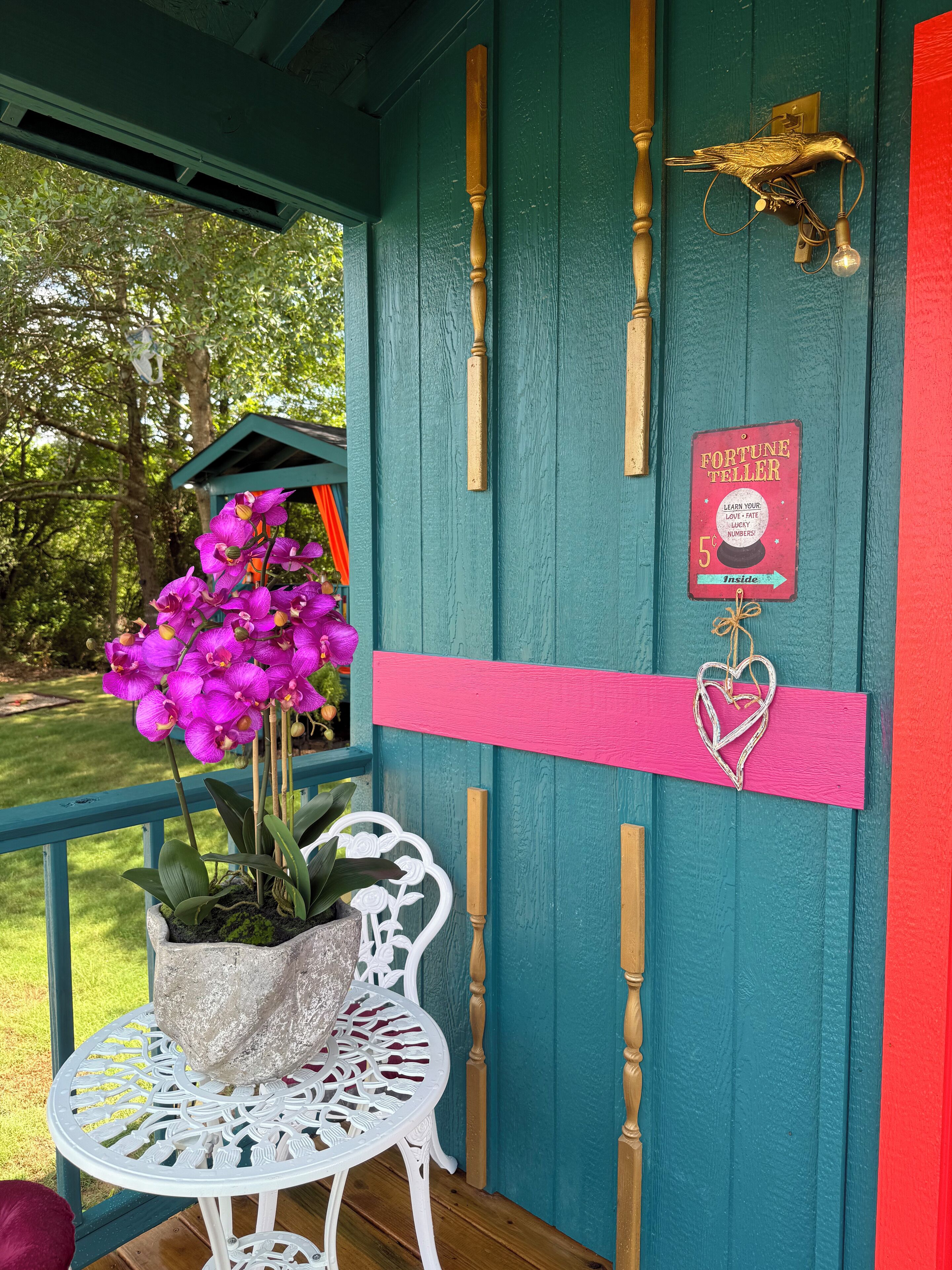 Una puerta color turquesa con un llamador de bronce con forma de pájaro, un letrero rojo y una decoración con forma de corazón.