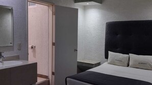 A bedroom with a bed, a bedside table, a mirror, and a ceiling fan. - Hotel Metropolitan (Guadalajara)