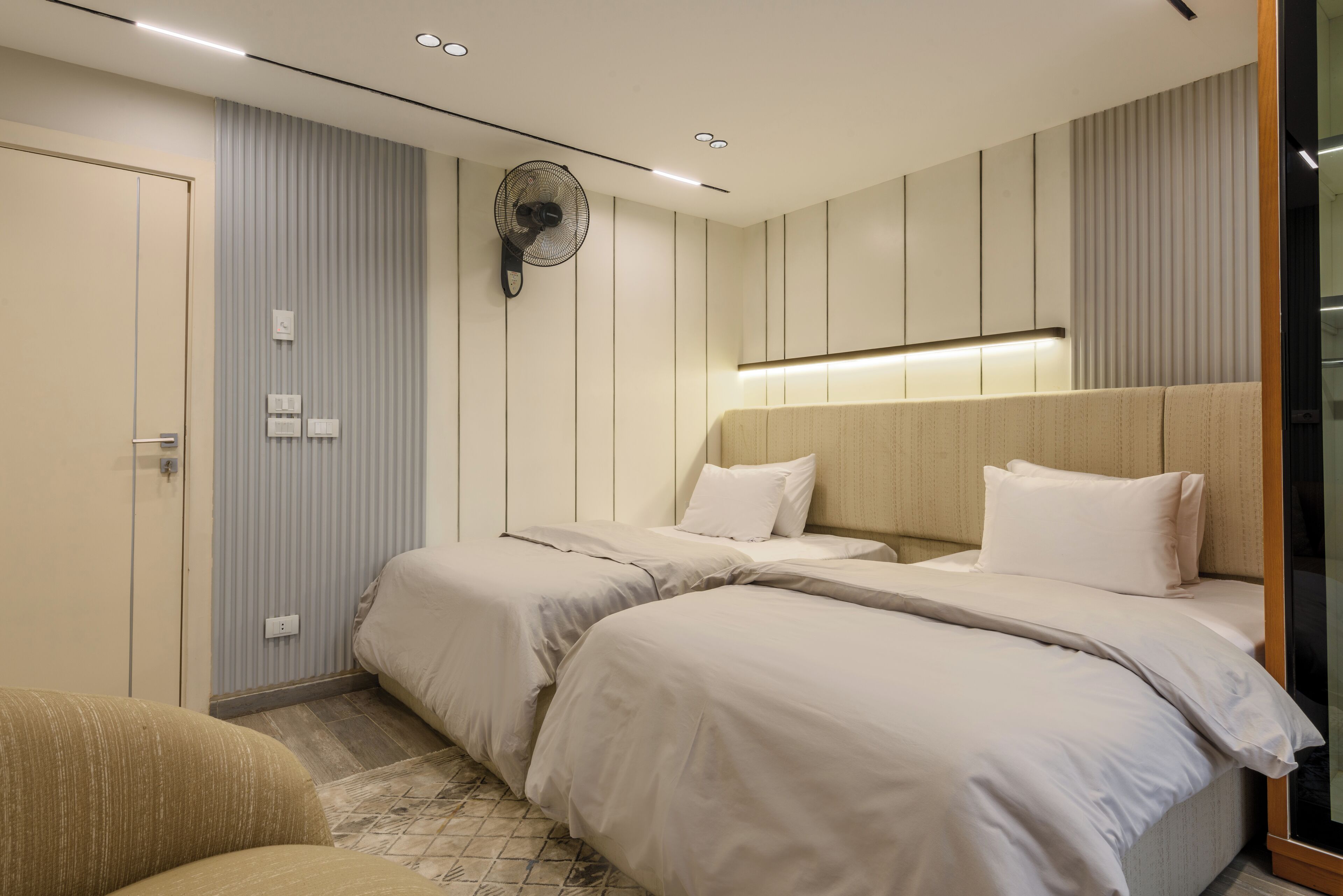 A hotel room with two beds, a wall-mounted fan, and a bedside table.