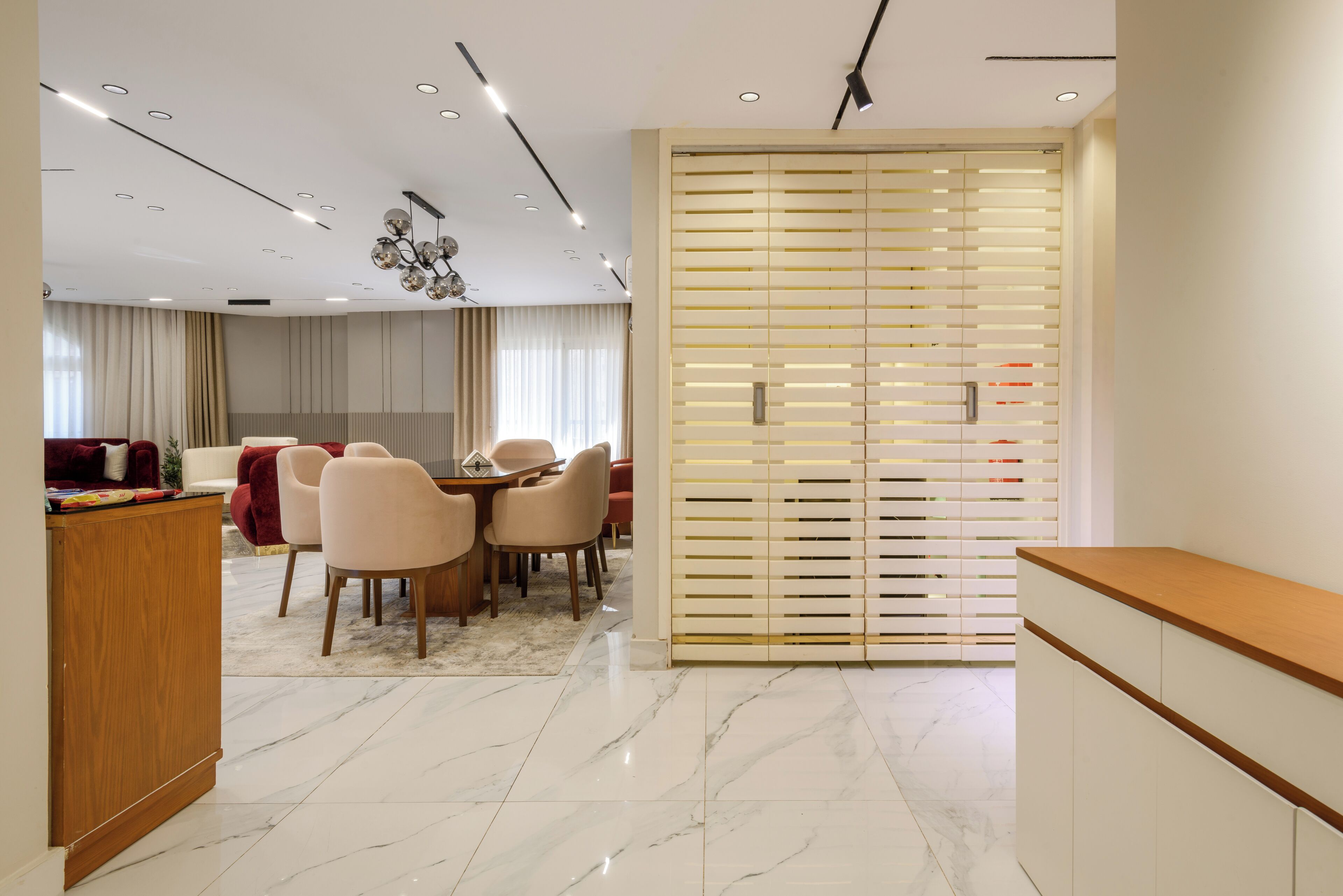 A modern dining area with a wooden table and chairs, a marble floor, and a decorative ceiling light fixture.