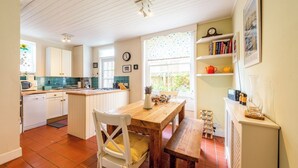 Una cocina con armarios blancos, una mesa de comedor de madera y una ventana con vistas a follaje.
