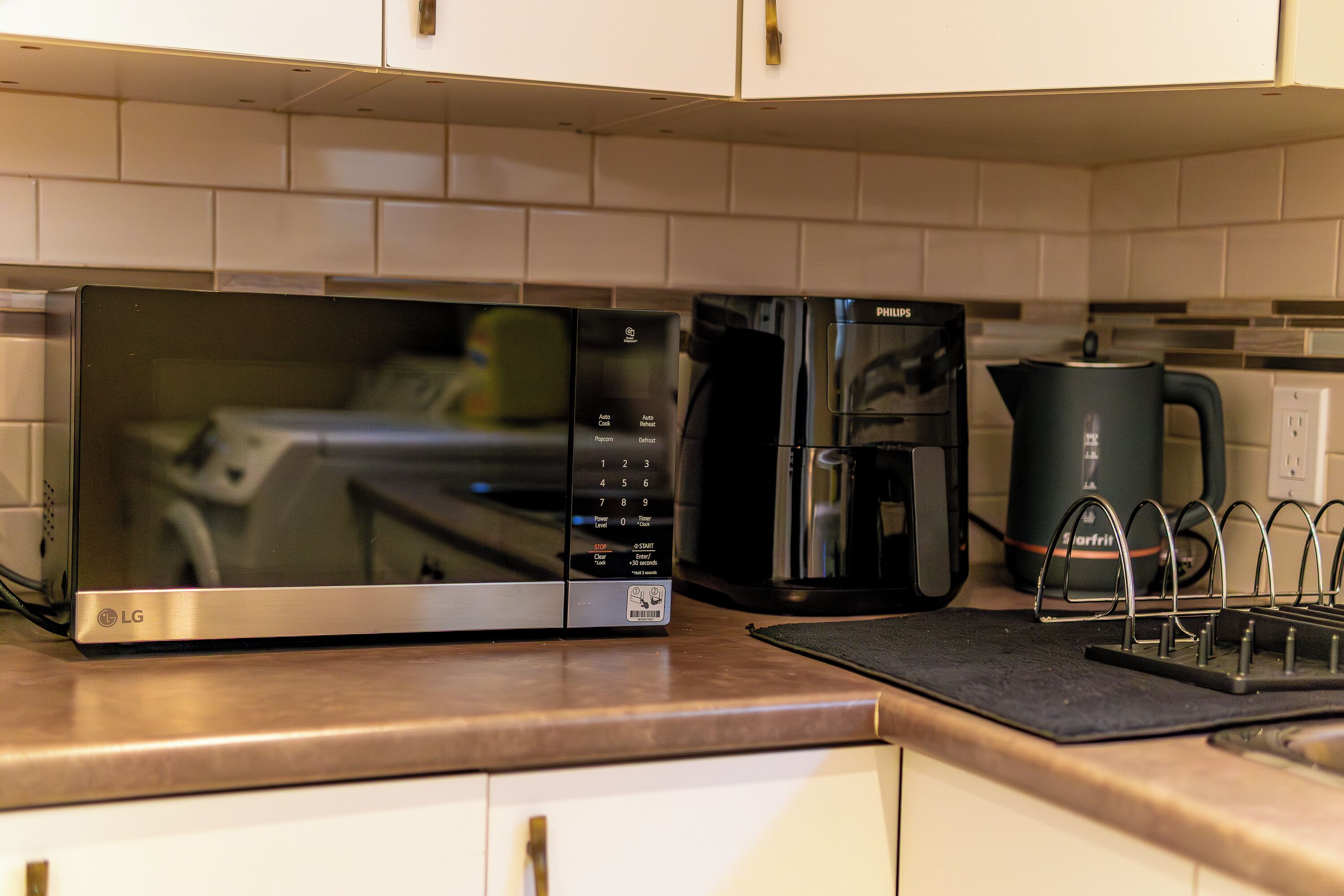 Une cuisine équipée d’un four à micro-ondes, d’une machine à café et d’une bouilloire, le tout posé sur le plan de travail.