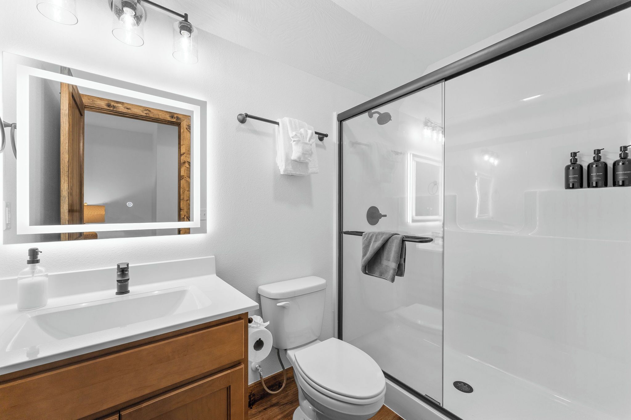 A modern bathroom with a white sink, wooden vanity, a glass shower enclosure, and a large mirror.