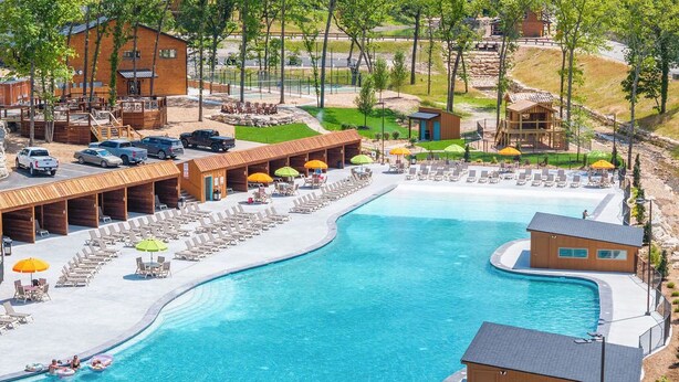 A resort with a large swimming pool, multiple lounge areas, and cabins. - Huck's Hollow | Hot Tub & Pools (Hollister)