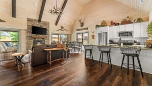 A spacious living area with a fireplace, a stone accent wall, and a large window. - Huck's Hollow | Hot Tub & Pools (Hollister)