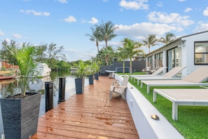 A wooden deck with lounge chairs and planters, overlooking a body of water and palm trees. - Tropical Waterfront Oasis with Hot Tub Jacuzzi (Dania Beach)