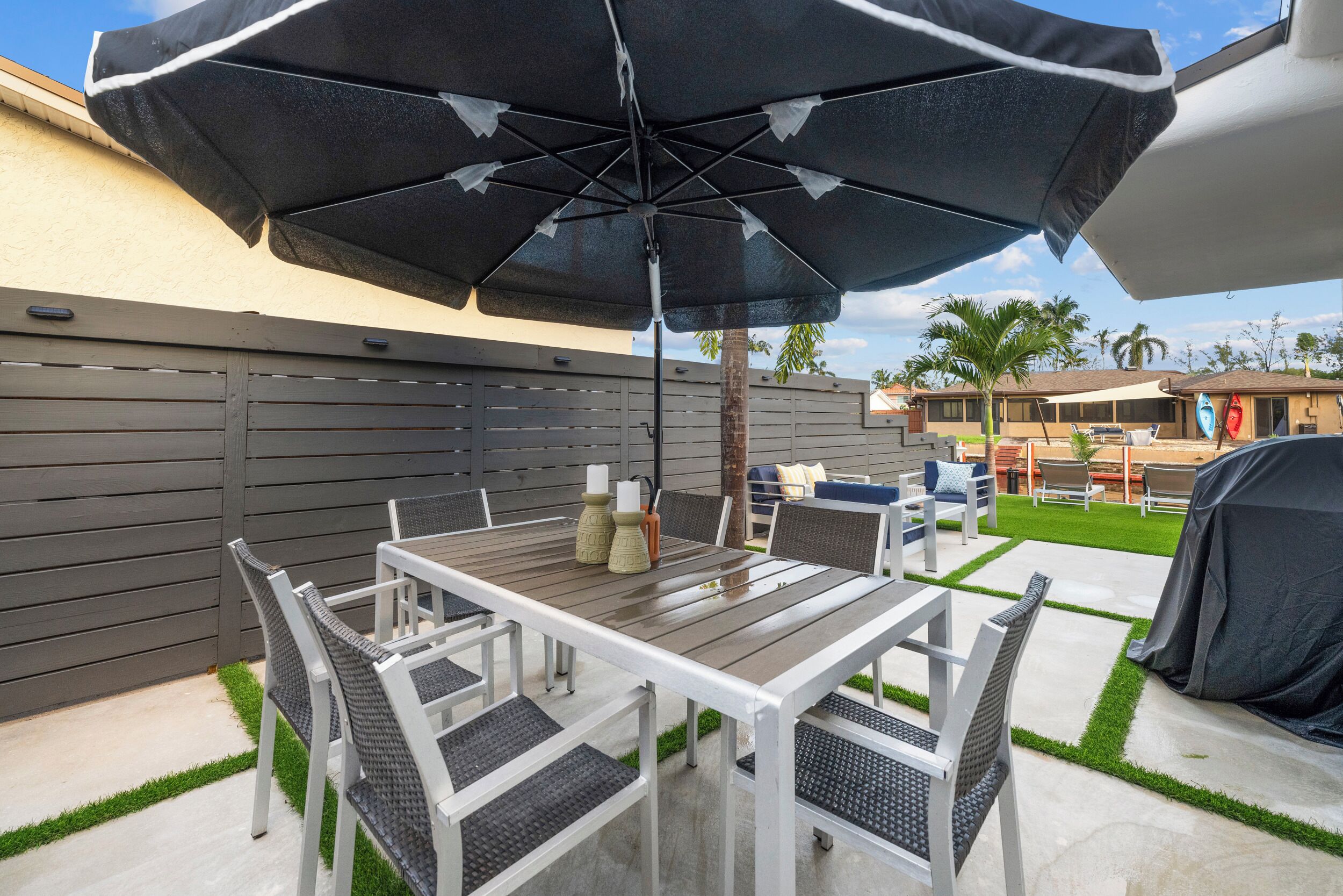 Une terrasse extérieure avec une table et des chaises, un grand parasol et un espace barbecue.