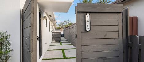 A narrow pathway leading to a gated entrance with a house number sign.