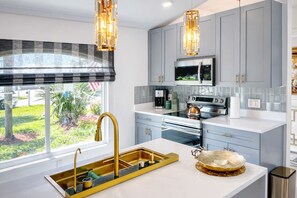 A modern kitchen with grey cabinets, stainless steel appliances, a gold faucet, and pendant lights.