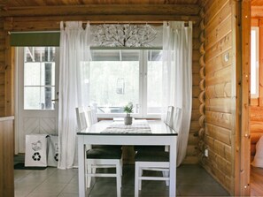 Un coin repas avec une table et des chaises, une fenêtre avec des rideaux et une porte sur la droite.