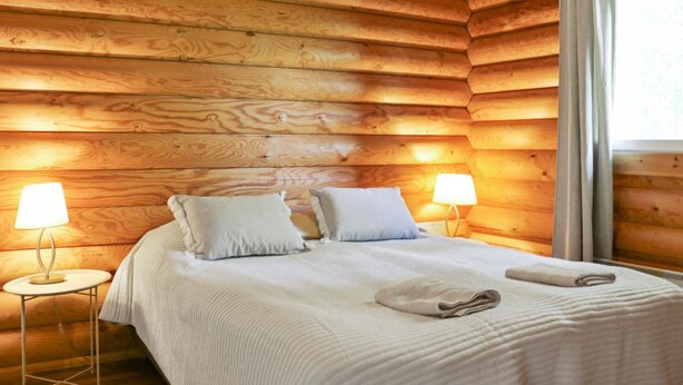 A wooden cabin room with a bed, two bedside lamps, and a window with curtains. - Vacation home Siili by Interhome (Savonlinna)