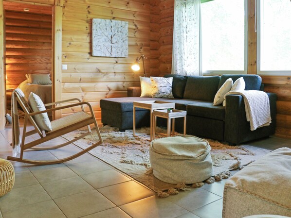A cozy cabin interior with a rocking chair, a sofa, a small table, and a rug on the floor.