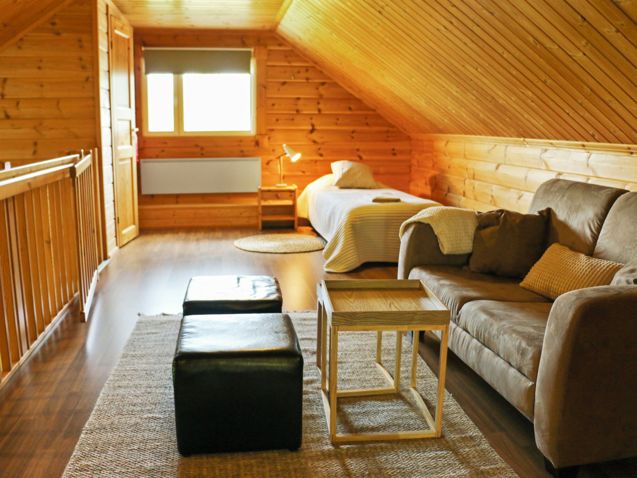 A cozy attic bedroom with a wooden sloped ceiling, a bed, a sofa, a nightstand, and a small table.