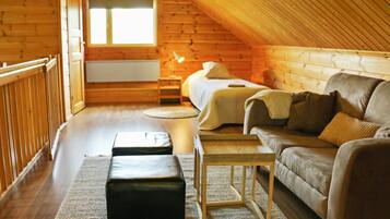 A cozy attic bedroom with a wooden sloped ceiling, a bed, a sofa, a nightstand, and a small table.