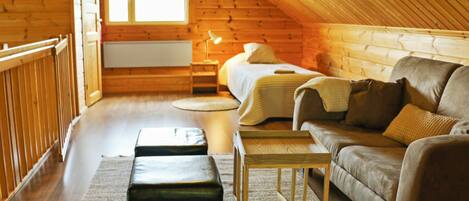 A cozy attic bedroom with a wooden sloped ceiling, a bed, a sofa, a nightstand, and a small table.