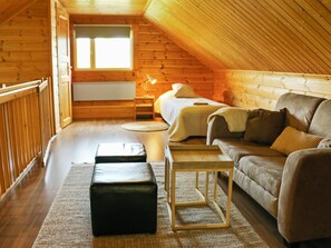 Une chambre mansardée chaleureuse avec un plafond en pente en bois, un lit, un canapé, une table de chevet et une petite table.