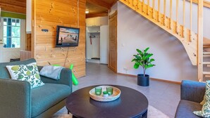 A wooden interior with a staircase, a sofa, a coffee table, and a potted plant.