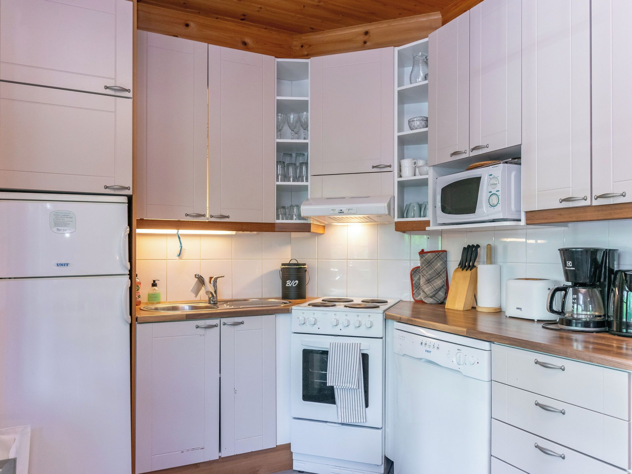 Une cuisine compacte avec des meubles blancs, un four à micro-ondes encastré, une cuisinière et une machine à café.