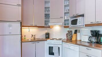 Une cuisine compacte avec des meubles blancs, un four à micro-ondes encastré, une cuisinière et une machine à café.