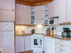 Una cocina compacta con armarios blancos, microondas integrado, estufa y cafetera.