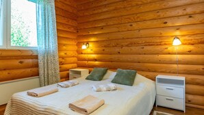 A cozy wooden cabin bedroom with a bed, two bedside tables, a nightstand, and a window with curtains.
