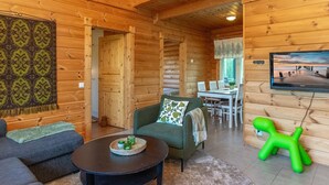 A cozy log cabin interior with a dining area, a television, and a green chair.