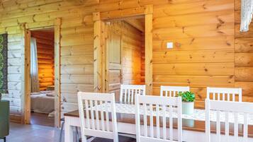 A wooden interior with a dining table and chairs, a potted plant, and a view of the outside.